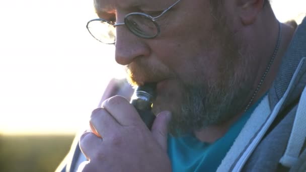 Volwassen bebaarde man zit in het park en elektronische sigaret roken — Stockvideo