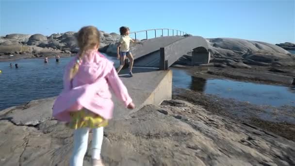 Twee kleine meisjes spelen onder de kust rotsen op het strand. — Stockvideo