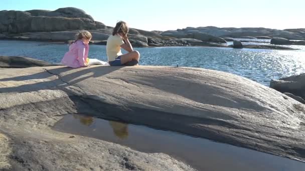 Дві маленькі дівчата грають серед прибережних скель на пляжі . — стокове відео