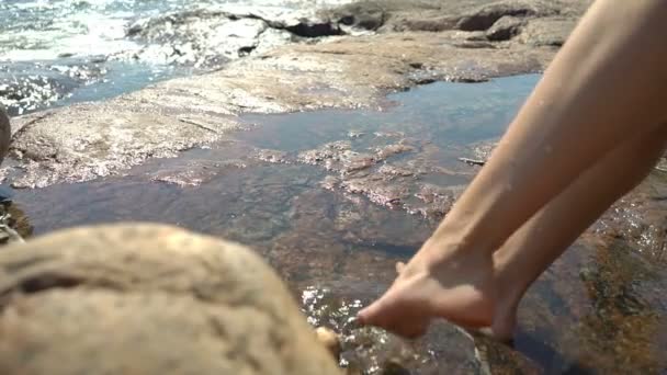 Eine junge Frau und ihre Tochter spielen in Felspfützen zwischen den Küstenfelsen am Strand — Stockvideo