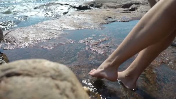 Eine junge Frau und ihre Tochter spielen in Felspfützen zwischen den Küstenfelsen am Strand — Stockvideo