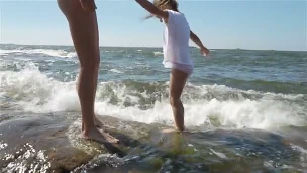 Una joven y su hija caminando y jugando con las olas del mar entre las rocas costeras — Vídeo de stock