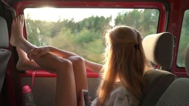 En ung rödhårig kvinna tycker om reser med bil kastar benen på fönstret. — Stockvideo