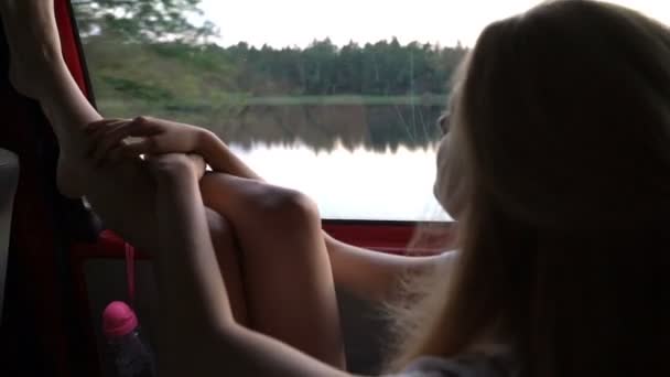 Una giovane rossa si diverte a viaggiare in auto getta le gambe sul finestrino . — Video Stock