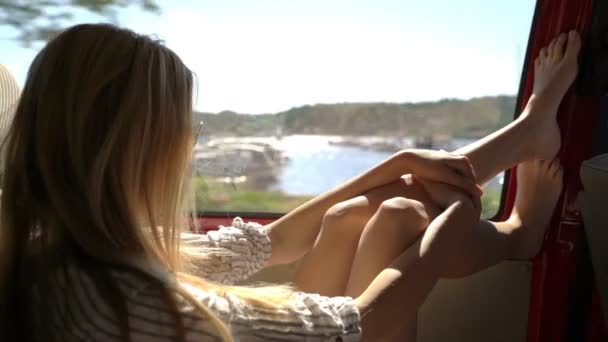 Una joven pelirroja disfruta viajando en coche arroja sus piernas por la ventana . — Vídeo de stock