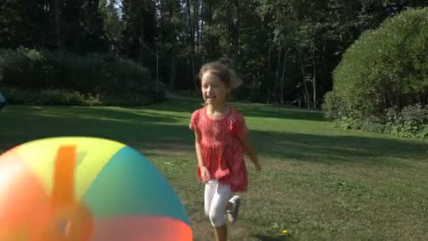 Linda niña jugando con una gran bola inflable de arco iris colorido — Vídeos de Stock