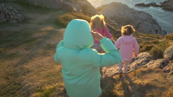 Zwei kleine Mädchen und ihre Mutter spazieren an einer felsigen Nordküste. — Stockvideo