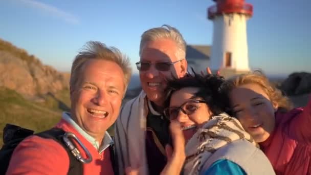 Eine große glückliche Familie macht ein Selfie oder benutzt eine Telefon-Videokamera an der Küste mit einem alten Leuchtturm — Stockvideo