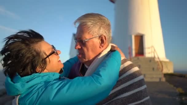Reifes Paar bei Sonnenuntergang am Meeresufer, das sich mit einem Plaid vor dem starken Wind bedeckt — Stockvideo