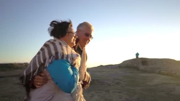 Äldre par promenader i solnedgången på stranden med en gammal fyr — Stockvideo