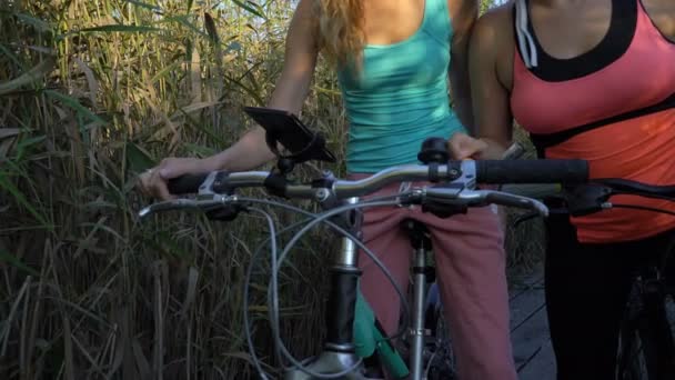 Duas jovens mulheres usam a navegação GPS no smartphone de bicicleta enquanto andam de bicicleta — Vídeo de Stock