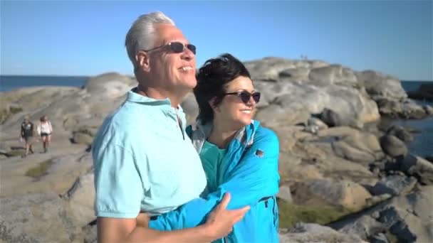 Una feliz pareja madura disfruta de un paseo entre las piedras costeras en la orilla del mar . — Vídeos de Stock