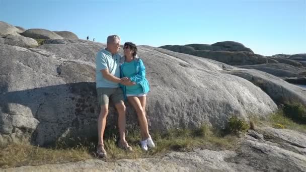 Um feliz casal amável e maduro desfruta de um passeio entre as pedras costeiras na costa . — Vídeo de Stock