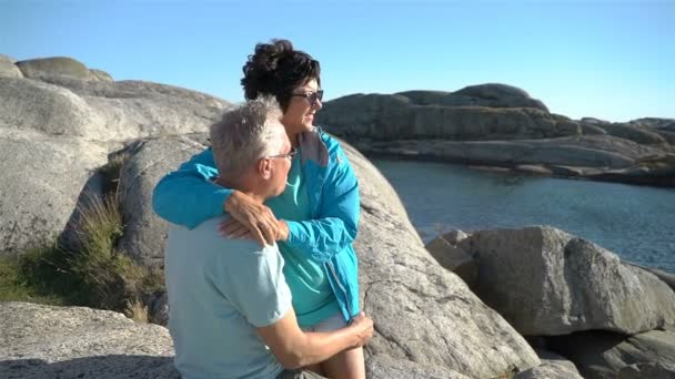 Um feliz casal amável e maduro desfruta de um passeio entre as pedras costeiras na costa . — Vídeo de Stock