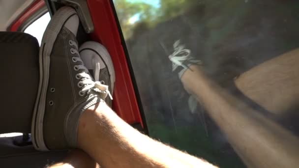 Um jovem gosta de viajar de carro joga suas pernas na janela . — Vídeo de Stock