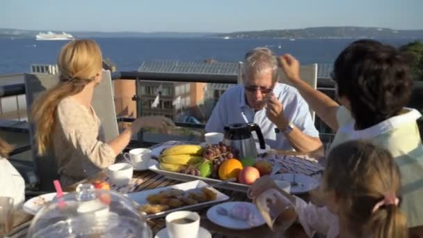 Una grande famiglia felice cena sulla terrazza aperta e saluta le mani passando vicino al traghetto di mare — Video Stock