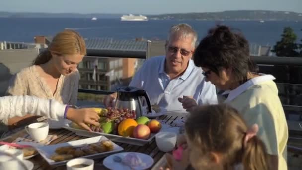 Uma grande família feliz janta no terraço aberto no telhado da casa . — Vídeo de Stock