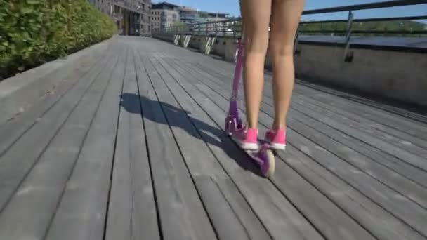 Tonårig flicka rider en Kick Scooter på strandpromenaden trä. — Stockvideo