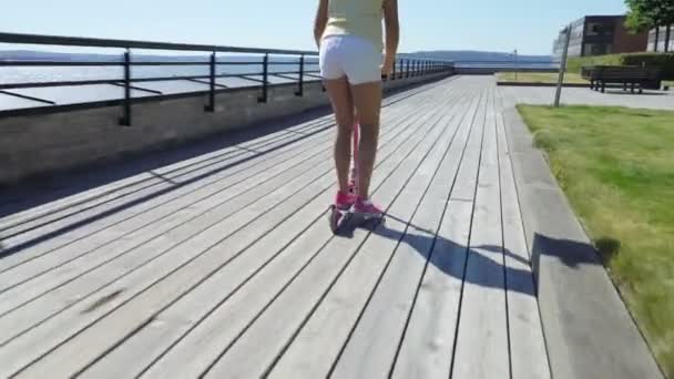 Teenager fährt mit Tretroller auf der Holzpromenade. — Stockvideo