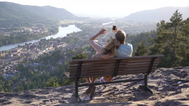 Casal amoroso romântico sentado no banco de madeira e admirando a cidade eo rio no vale — Vídeo de Stock