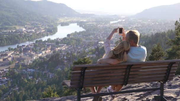 Romántica pareja amorosa sentada en un banco de madera y admirando la ciudad y el río en el valle — Vídeos de Stock