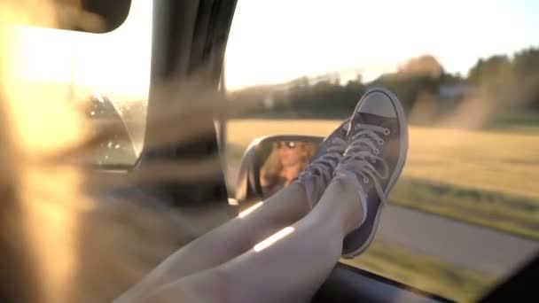 A young woman enjoys traveling in a car by sticking out her legs in an open window — Stock Video