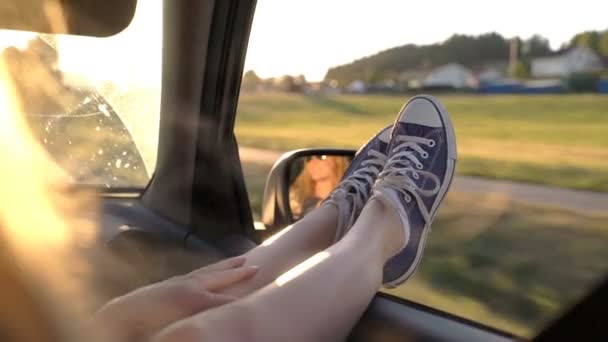 A young woman enjoys traveling in a car by sticking out her legs in an open window — Stock Video
