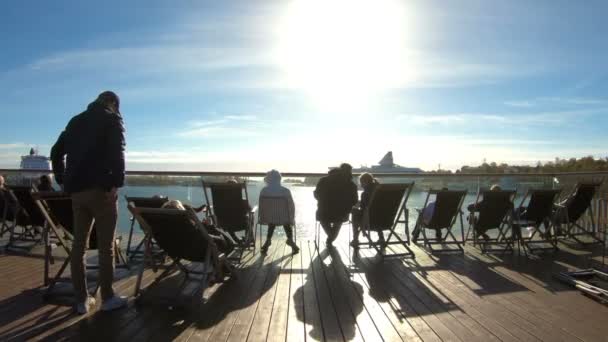 Människor njuta de sista soliga dagarna sitter i en solstol på strandpromenaden i höst i Helsingfors, Finland — Stockvideo