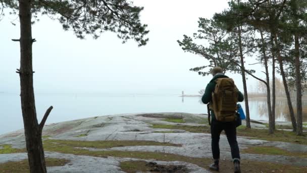 Ein Mann mittleren Alters beobachtet an einem nebligen Herbstmorgen die Tierwelt durch ein Fernglas an einem felsigen Ufer des Meeres. — Stockvideo