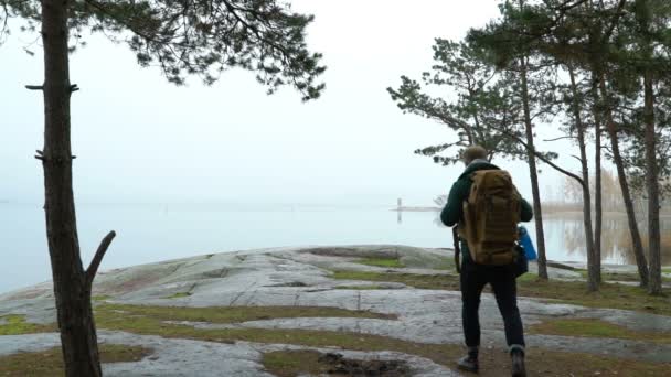 En medelålders man titta på vilda djur genom kikare på en stenig strand i havet på en dimmig höst morgon. — Stockvideo