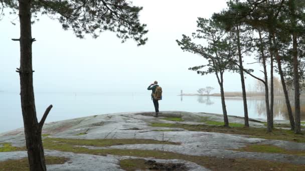 Un uomo di mezza età che osserva la fauna selvatica attraverso un binocolo su una riva rocciosa del mare in una nebbiosa mattina d'autunno . — Video Stock