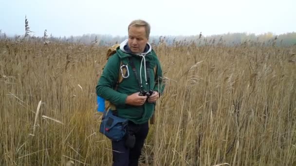 Un hombre de mediana edad con una mochila pasa por las cañas — Vídeo de stock