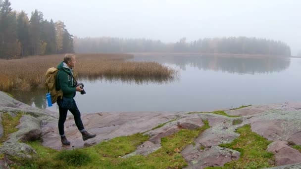 Un hombre de mediana edad con una mochila fotografiando vida silvestre en una costa rocosa — Vídeo de stock