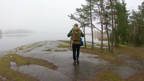 Ein Mann mittleren Alters beobachtet an einem nebligen Herbstmorgen die Tierwelt durch ein Fernglas an einem felsigen Ufer des Meeres. — Stockvideo