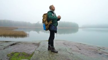 Orta yaşlı bir adam bir sisli sonbahar sabahı kayalık deniz kıyısında dürbün ile yaban hayatı izliyor.