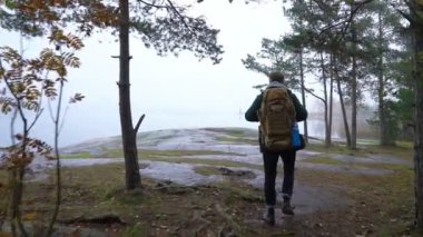 Orta yaşlı bir adam bir sisli sonbahar sabahı kayalık deniz kıyısında dürbün ile yaban hayatı izliyor.