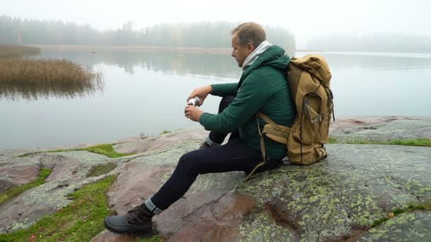 バルト海の岩の海岸に座っているバックパックと中年男. — ストック動画