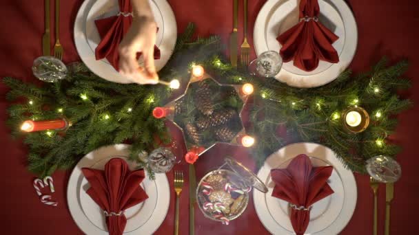 Female hand lights christmas candles. Festive red table setting with garland. — Stock Video