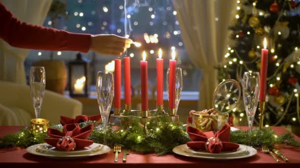 La mano femenina enciende velas de Navidad. Mesa roja festiva con guirnalda . — Vídeos de Stock