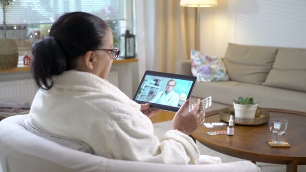 Медицина онлайн. Літня жінка консультується зі своїм лікарем, використовуючи відеочат вдома — стокове відео