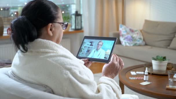 Medizin online. ältere Frau berät sich mit ihrem Arzt per Videochat zu Hause — Stockvideo