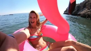 Denizin ve güneşin bir şişme Pembe Flamingo üzerinde yalan genç ince kadın seviyor