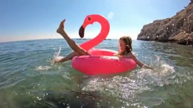 Denizin ve güneşin bir şişme Pembe Flamingo üzerinde yalan genç ince kadın seviyor