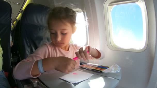 Une petite fille voyageant en avion et dessinant une image avec des crayons colorés . — Video