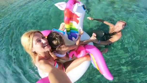 Familia feliz con la muchacha que toma selfie en los asientos del mar en el unicornio inflable — Vídeo de stock