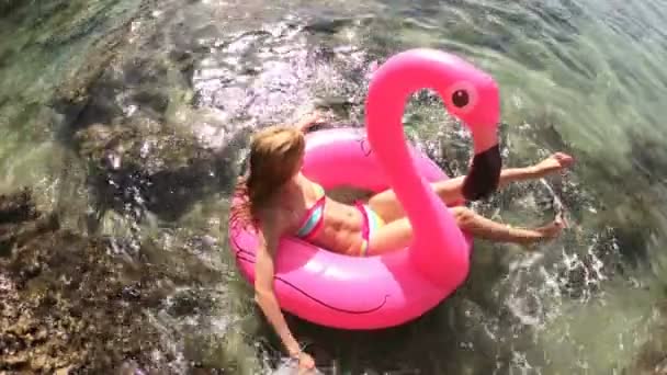 Giovane donna snella gode il mare e il sole sdraiato su un fenicottero rosa gonfiabile — Video Stock