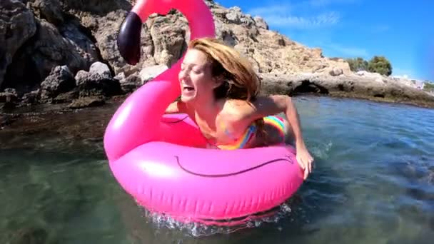 Νεαρή λεπτή γυναίκα απολαμβάνει τη θάλασσα και τον ήλιο, ξαπλωμένη σε ένα φουσκωτό ροζ φλαμίνγκο — Αρχείο Βίντεο
