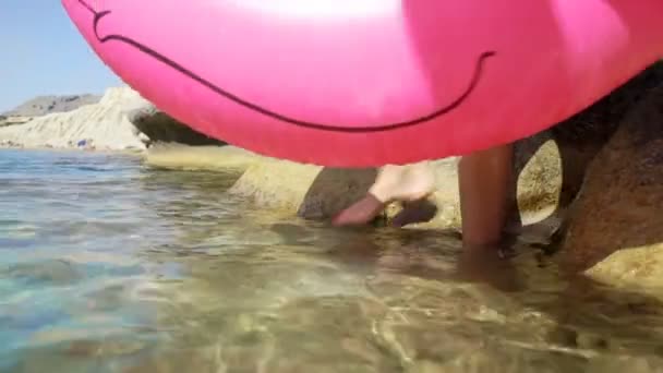 Giovane donna snella gode il mare e il sole camminando in acqua con un fenicottero gonfiabile rosa — Video Stock