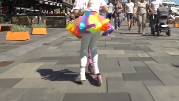 A kicsi lány egy szoknya világos rainbow és a sisak lovagol egy robogó, többek között a város tömeg, Oslo. — Stock videók