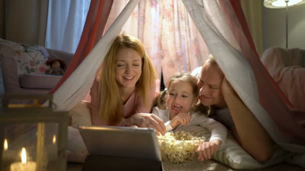 Holčička a její rodiče si sledoval karikatury online ve stanu v dětském pokoji — Stock video
